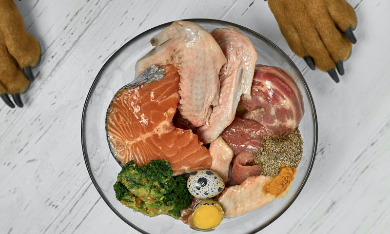 Raw chicken salmon and beef in a glass bowl with broccoli quail egg and spices