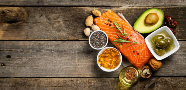 Food spread on a wooden plank of raw salmon, bowl of omega 3, eggs, half an avocado, chia seeds, and pecans.