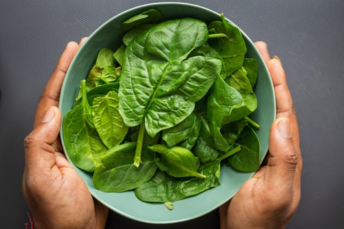 Man holding green ceramic bowl full of fresh green spinach