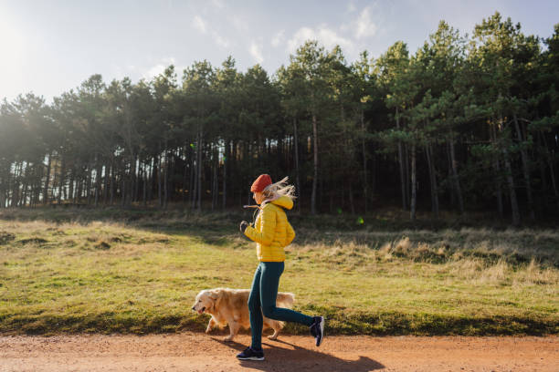 Lady in yellow jacket jogging with her dog through the forest