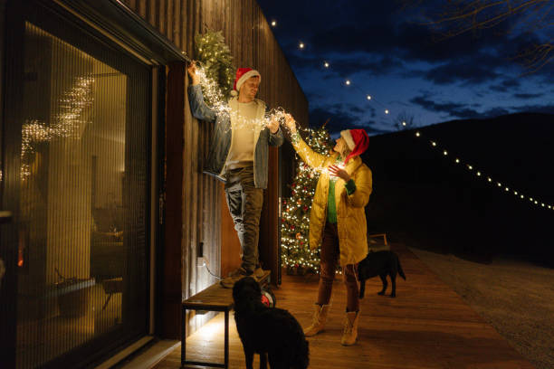 Couple decorating barn with christmas lights while their dog watches