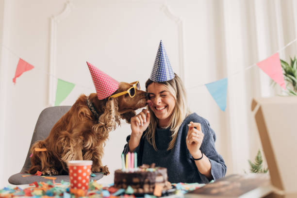 Owner celebrating her dog's birthday, they are both wearing hats, there is confetti and a cake